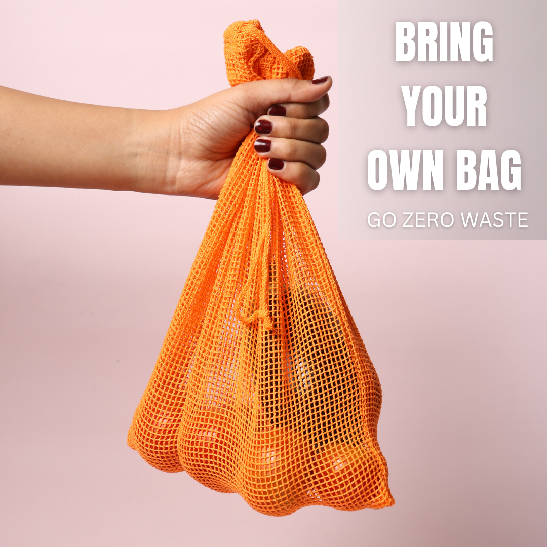 Hand holding an orange mesh bag with text 'Bring Your Own Bag, Go Zero Waste' on a pink background PT-MSH-ORG