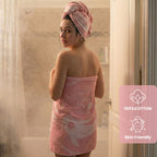 Woman wrapped in a pink towel with a towel rack in the background, featuring a '100% Cotton' and 'Skin Friendly' label. VU-YNG-RSE