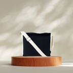 Black bag with a white strap on a wooden platform against a neutral background NC-DMC-BLK