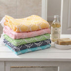 Stack of colorful towels on a table with a bottle of shampoo and soap. VU-OCN-IND VU-OCN-SEA VU-OCN-CRL VU-OCN-SUN VU-OCN-SAG